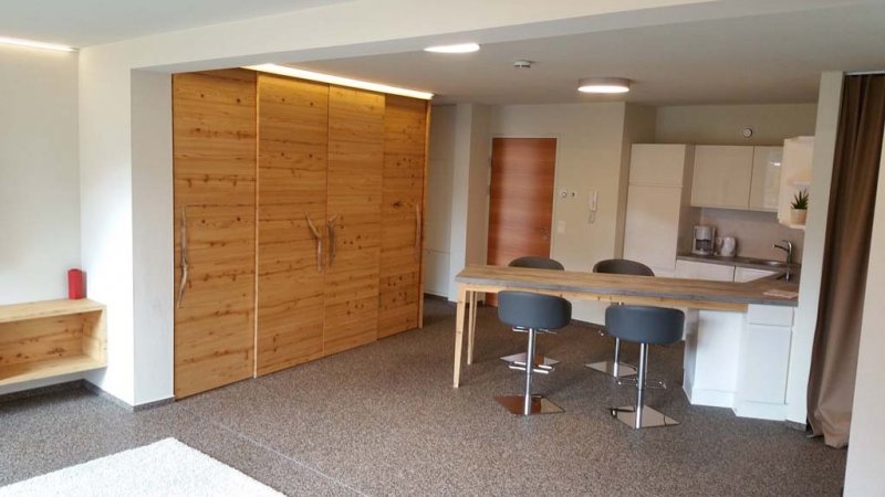 grosser-wohnraum-mit-holzschrank-und-gemuetlichen-barhockern-an-der-theke